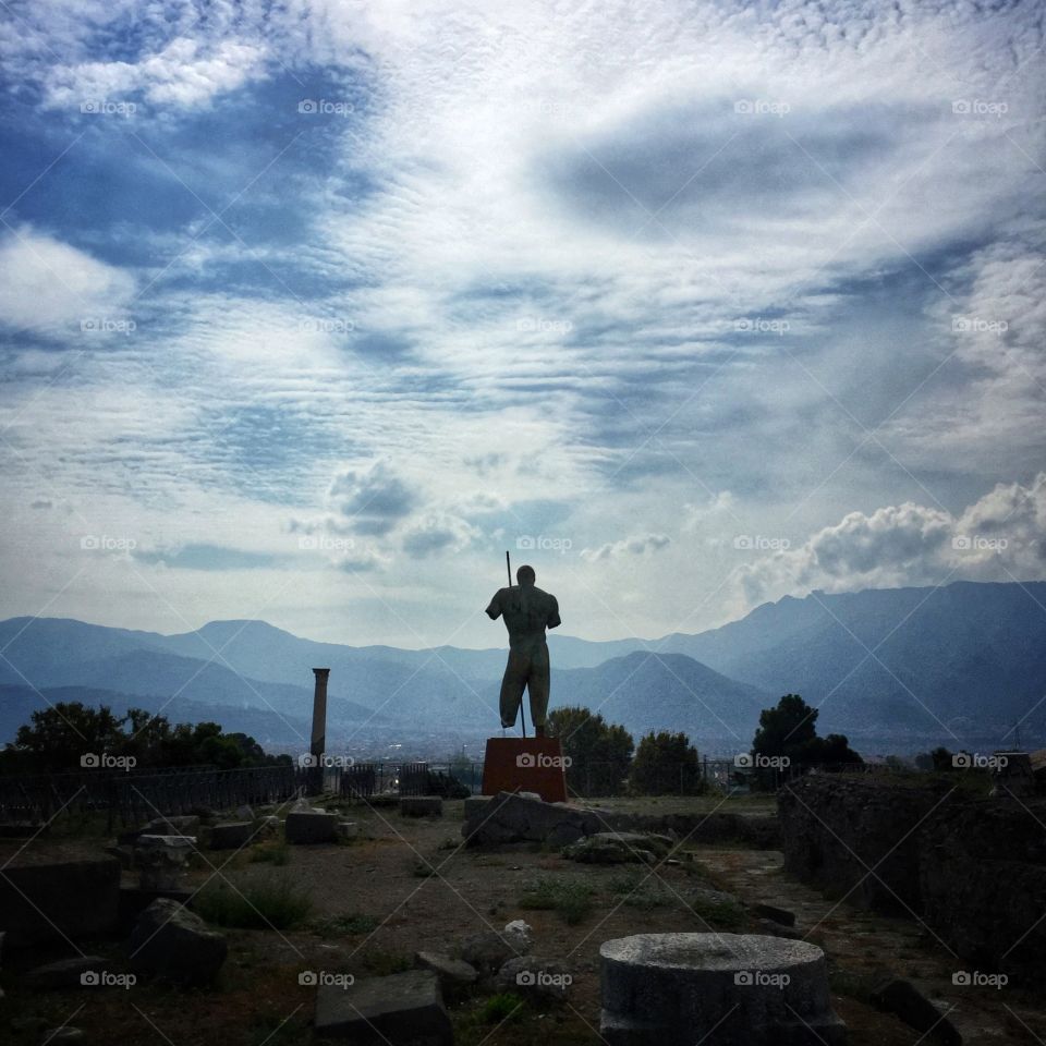 Bronze statue of Apollo facing away from the ruins of Pompeii 