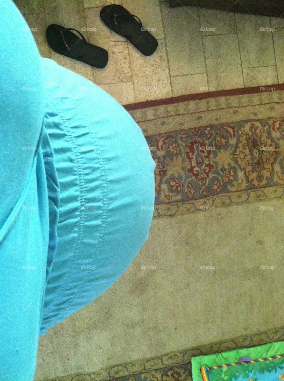 Mother-to-be in a blue dress looking downward at her 9 month baby bump. 