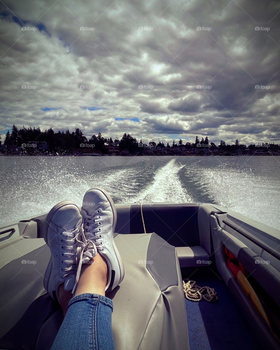 A pair of feet are propped up in a speedboat as it cruises on a clear blue lake, relaxing days abound