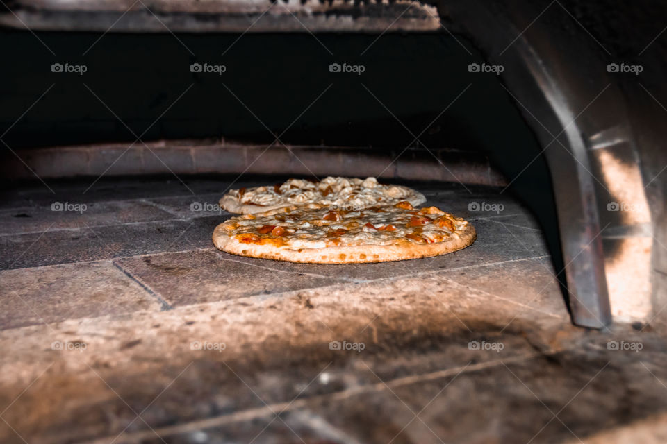 Two pizzas being prepared in wood fired oven