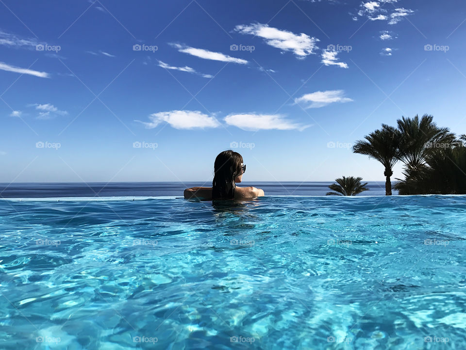 Young woman enjoying the beautiful view from the swimming pool above the sea 