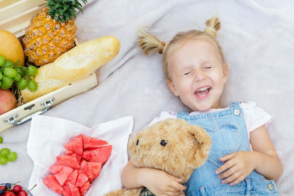 Happy little Caucasian girl with smiley face lying on picnic blanket 