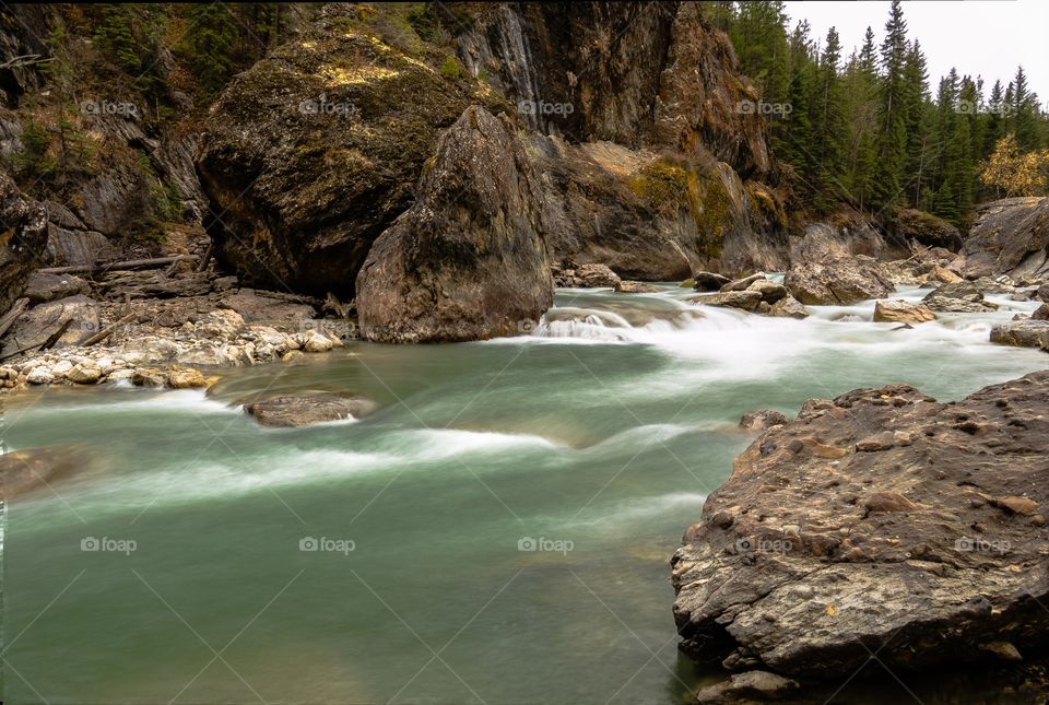Green creek flowing past boulders, long exposure