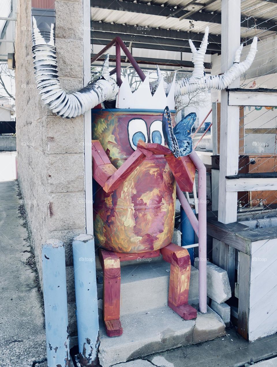 A tin can moose holding a butterfly, outside of a plant exchange.