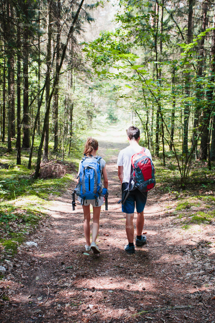 Young boy and girl wandering in a forest on summer day equipped with backpacks