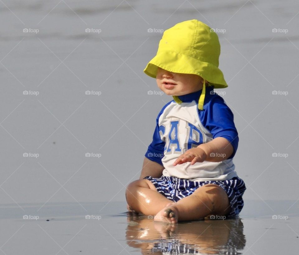 Baby on the beach wearing a bright yellow hat