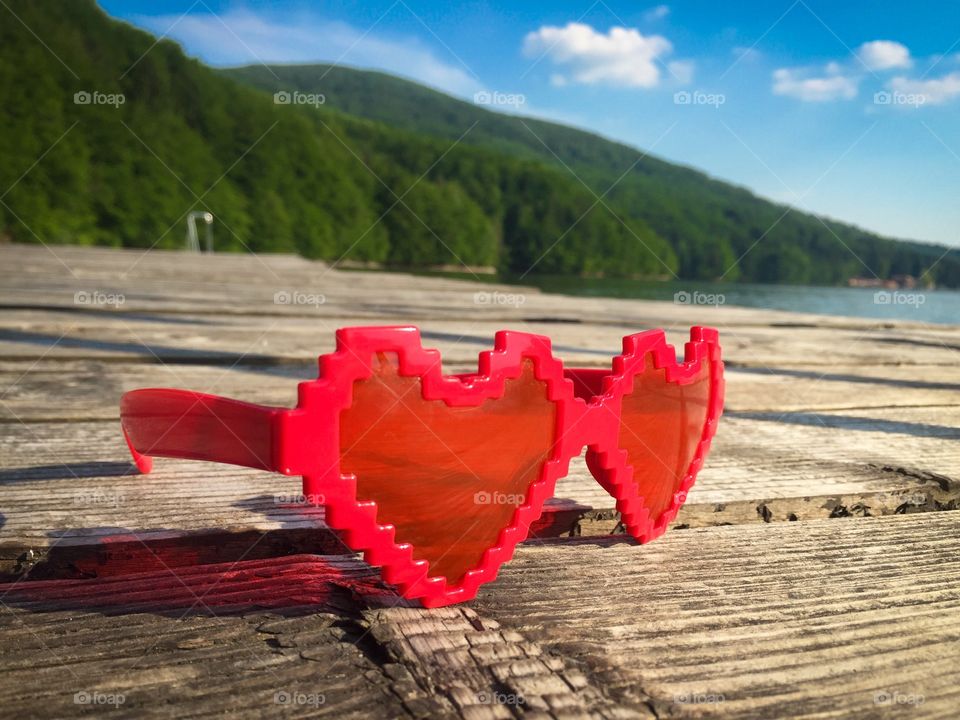 Heart shaped sunglasses on wooden pontoon near the lake