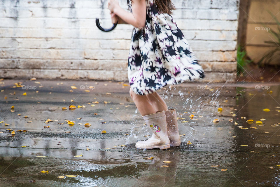 Water fun at home - girl playing, jumping and dancing in water puddles in the garden. Image of a girl splashing water with water boots and dress outside.