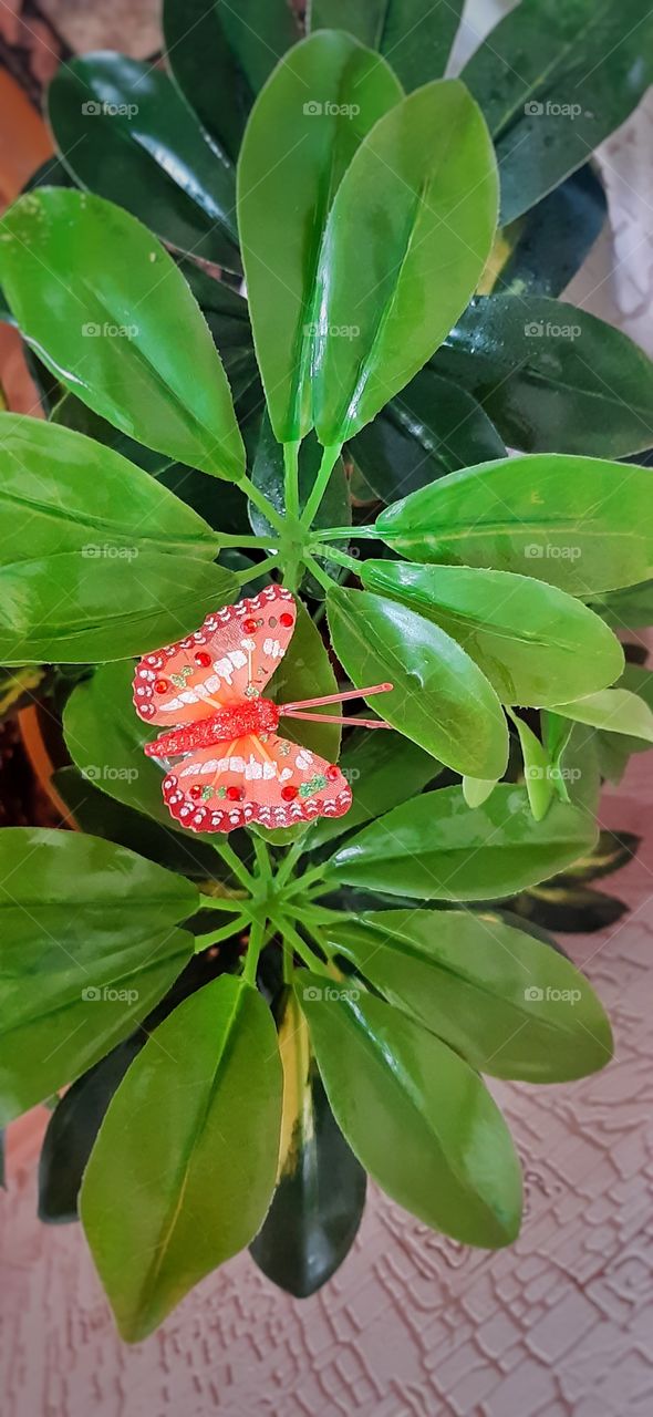 бабочка из красного бисера на зеленых листьях