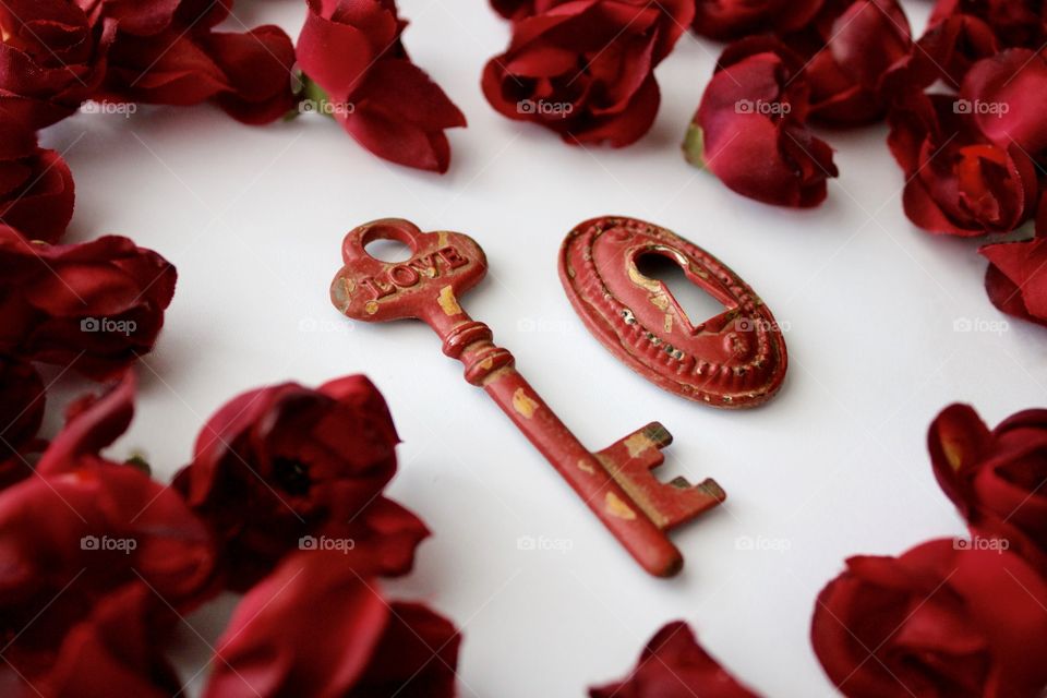 Red, metal, vintage key and keyhole with red, silk rose buds on white marble surface