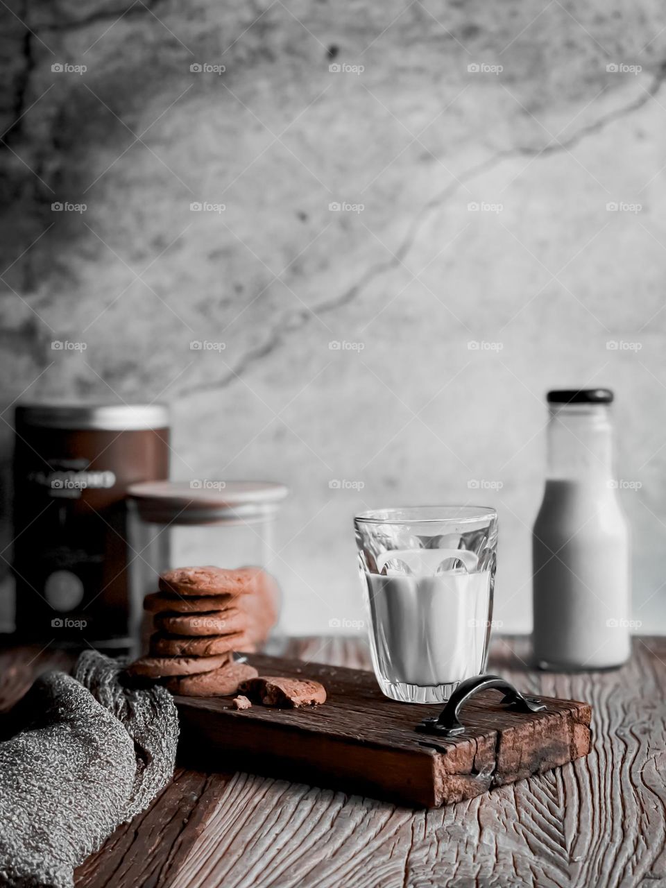 A cup of warm milk and stacks of biscuits on a wooden board and a bottle of milk at the back