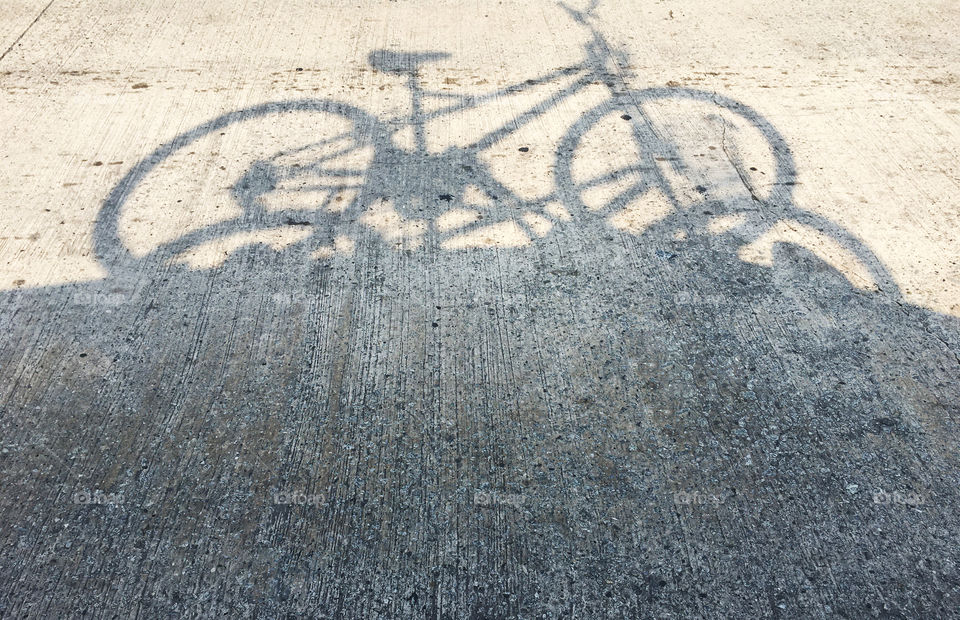 Shadow of a bicycle placed on top of the car and being taken to pedal on the beach.