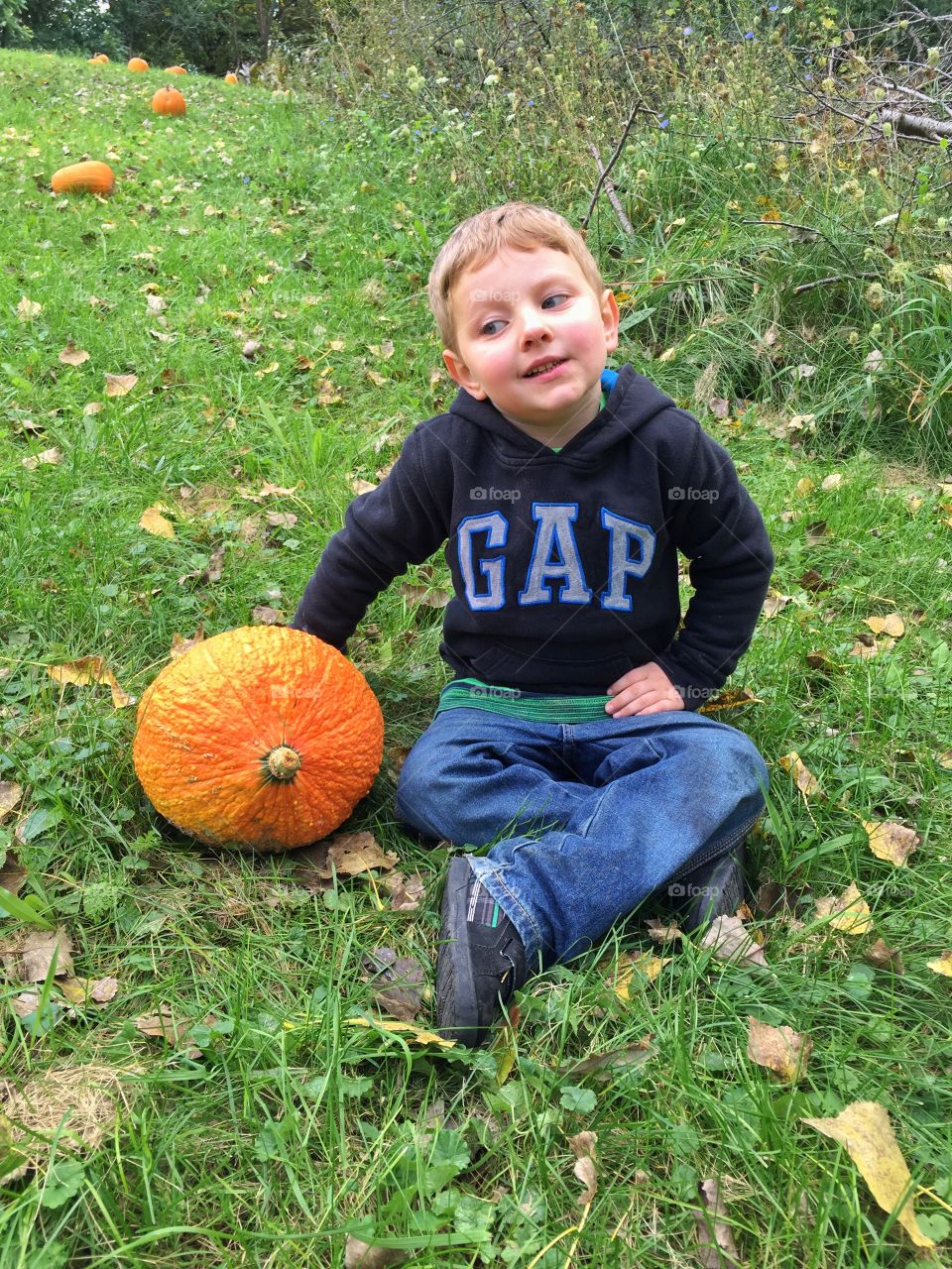 Boy sitting in field near pumpkin