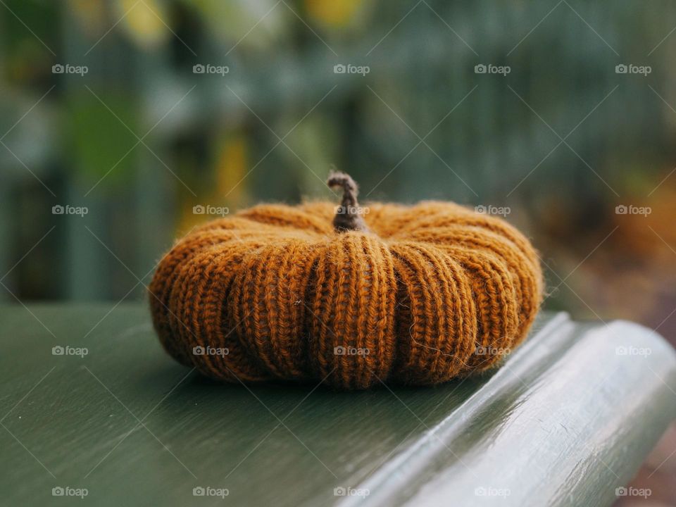 Handmade orange knitted Halloween pumpkin lies on a green bench in a autumn day, nobody 