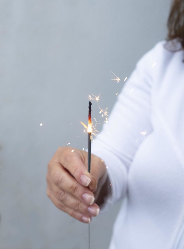 A woman dressed in white holds in hand a rocket candle giving a magical glow to her birthday
