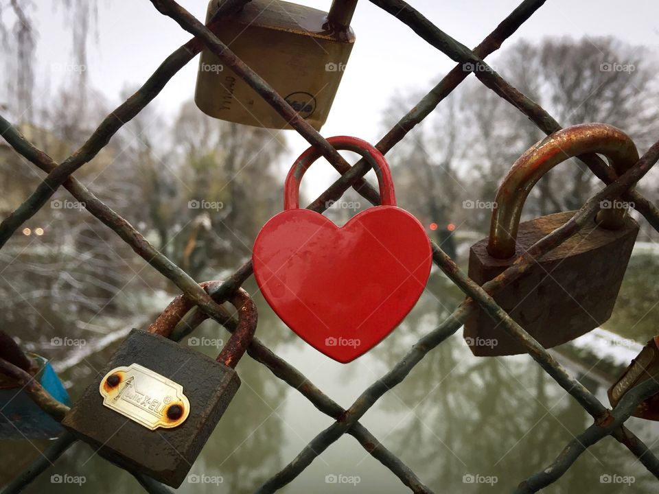 Red heart shaped padlock hanging on the bridge 
