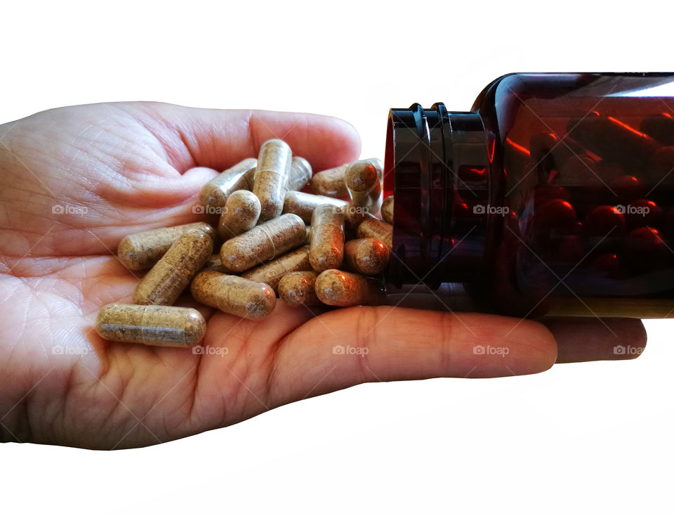 Herb supplement tablets spilling out of a brown plastic medicine bottle on human hand