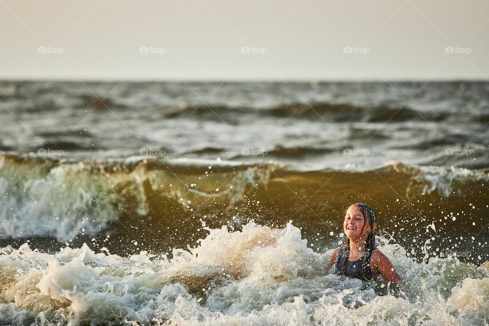 Little girl playing with waves in the sea. Kid playfully splashing with waves. Child jumping in sea waves. Summer vacation on the beach. Water splashes. Travel during summertime concept