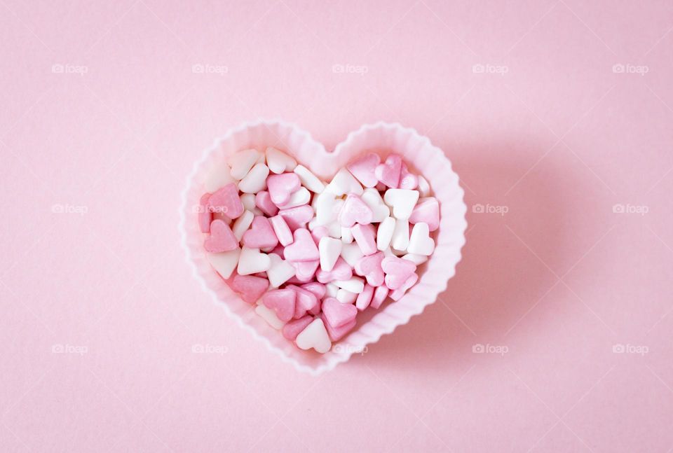 One silicone heart shape for baking muffins with candy sprinkles inside lies in the center on a soft pink background, flat lay close-up.