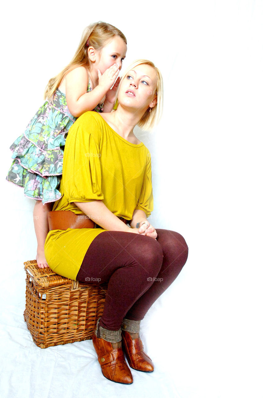 A YOUNG MOTHER LISTENS AS HER DAUGHTER WHISPERS IN HER EAR.