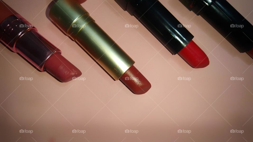 Close view of multiple lipsticks in parallel arrangements against a pink background.