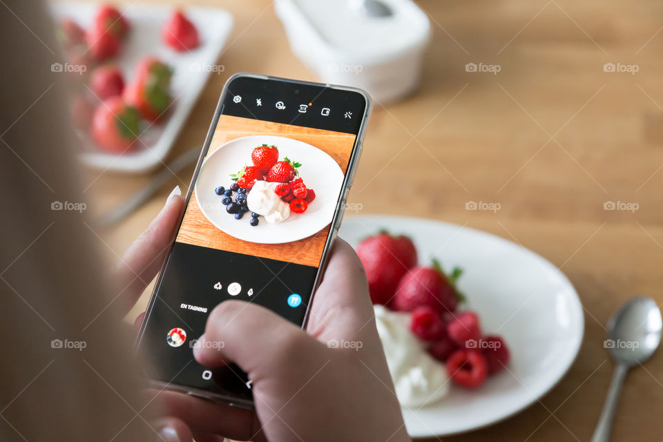 Woman taking a picture of a plate with fresh healthy berries and ice cream with the mobile phone 