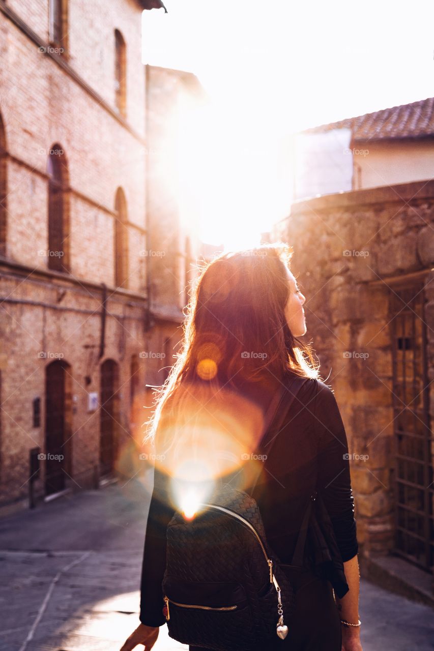 Rear view of woman walking in alley with sunlight