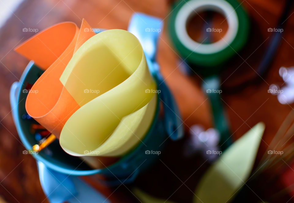Colored paper and tape roll from High angle view of arts and crafts supply wooden desktop work table with focus on foreground of colored papers organized in bucket