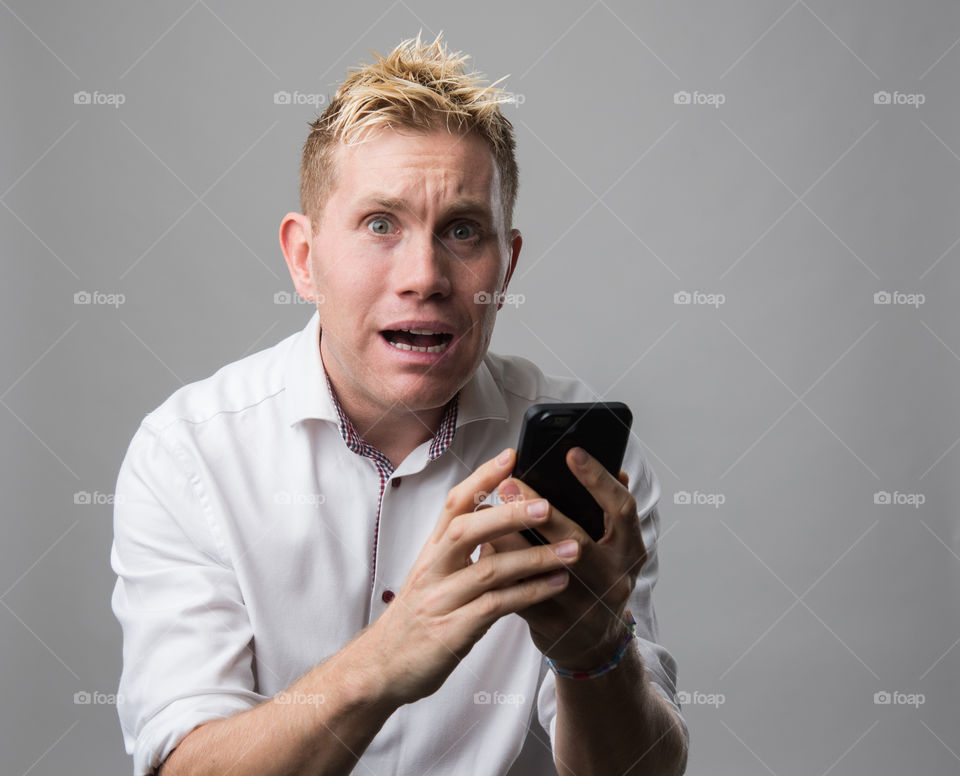 Man with celular phone surprised and horrified over something in the phone.