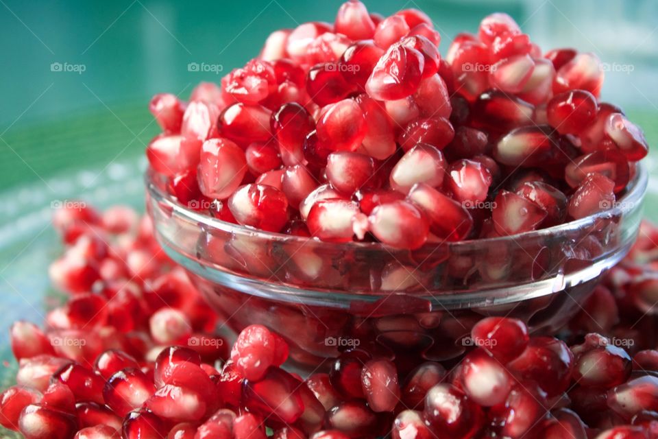 Fruits! - Closeup of fresh pomegranate seeds overflowing a small glass bowl against a green background