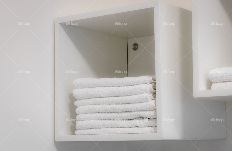 A stack of clean white and neatly folded towels lie in a wall-mounted open closet shelf in a hairdressing salon, close-up side view. The concept of white on white,monochrome, barbershop items