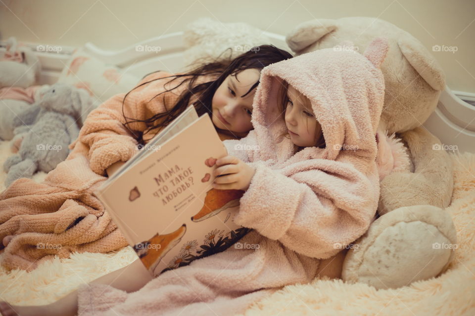 Little sisters in bathrobe reading the book