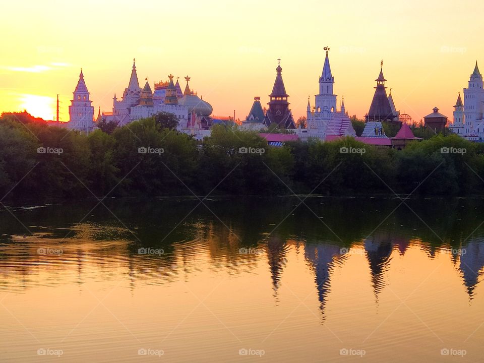 Summer sunset.  All shades of pink.  Treetops and tower domes are reflected in the water.  The sun sets behind the domes and the walls of the fortress are painted in all shades of pink