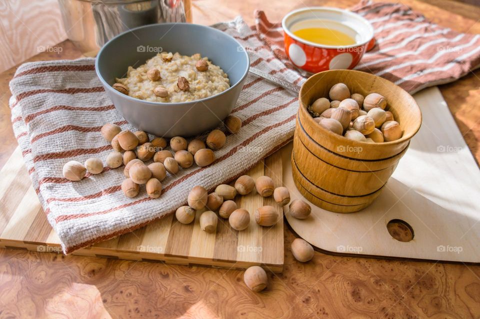 Cooked oatmeal in a deep gray plate with hazelnuts and honey.
