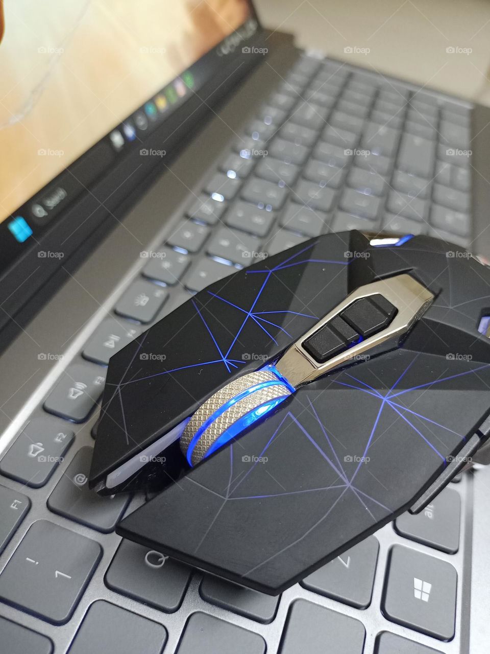 RGB Gaming mouse above silver laptop keyboard black gaming mouse with fancy light