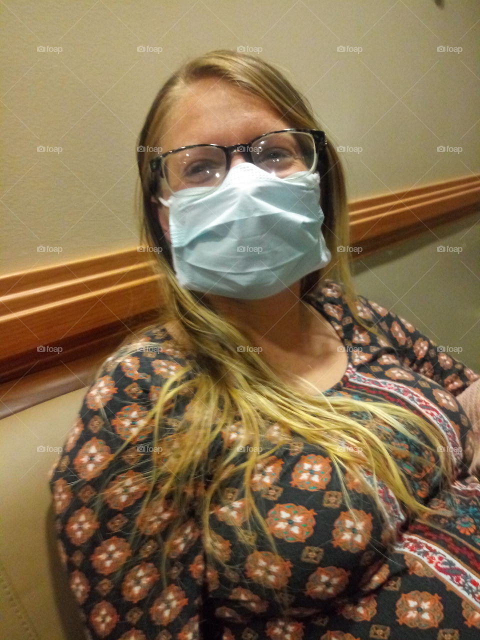 a young pregnant woman wearing glasses and a facemask in public due to covid.