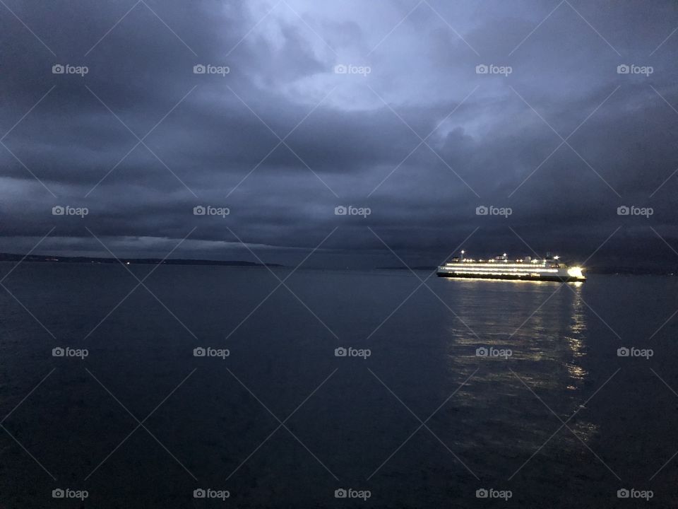 The lit ferry with the backdrop of the gray storm clouds in the backdrop gives an eerie feeling and makes it look haunted 