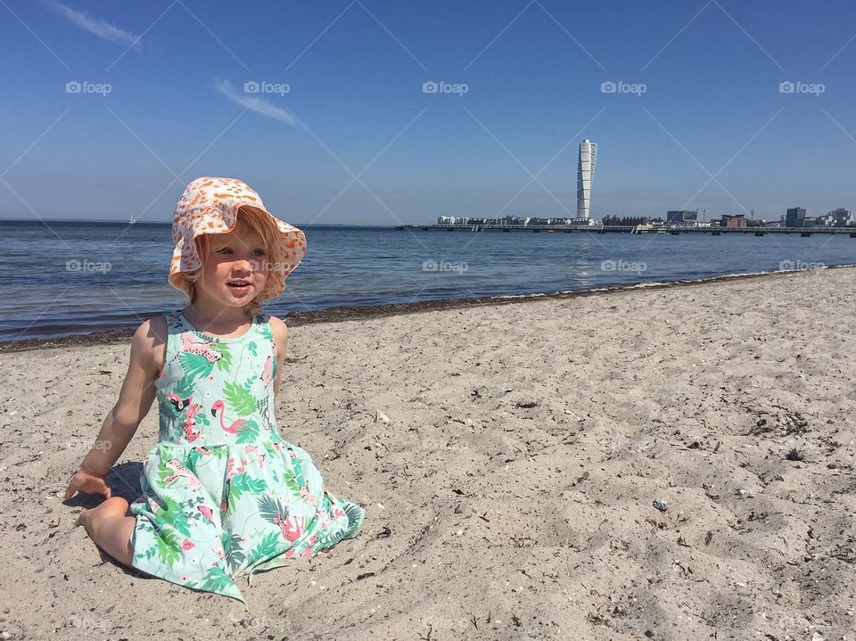 Little girl of three years old playing in the sand at Ribban bech in Malmö Sweden with the famous skyscraper Turni g Torso in the background.