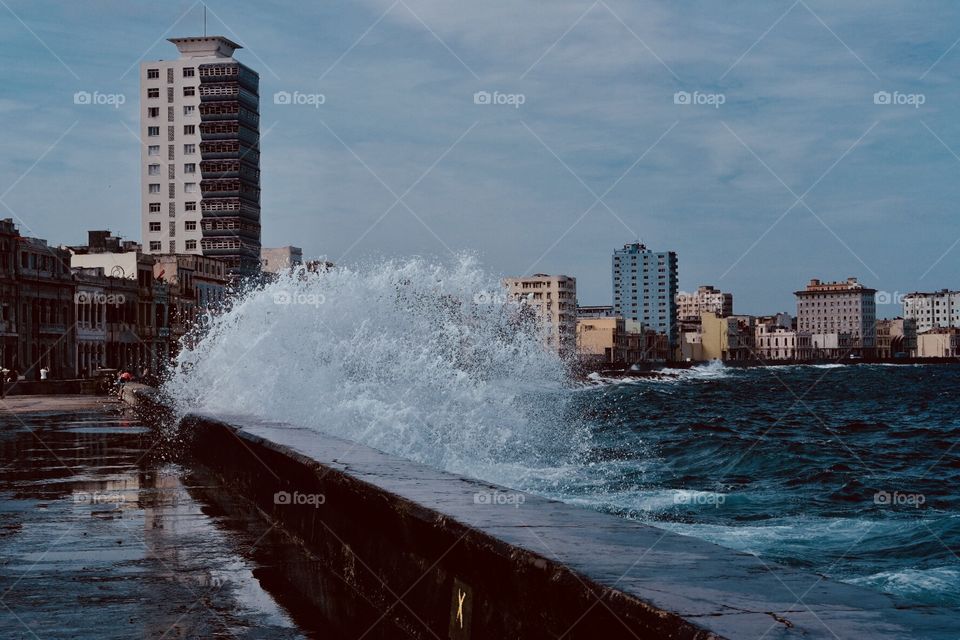 A big wave hitting the road with the view of the city behind 