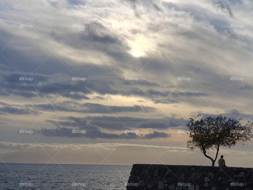 evening clouds at the sea - one man sitting next to a tree and is dreaming