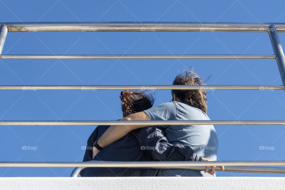 Back view of woman and man embraced on a ship against blue sky