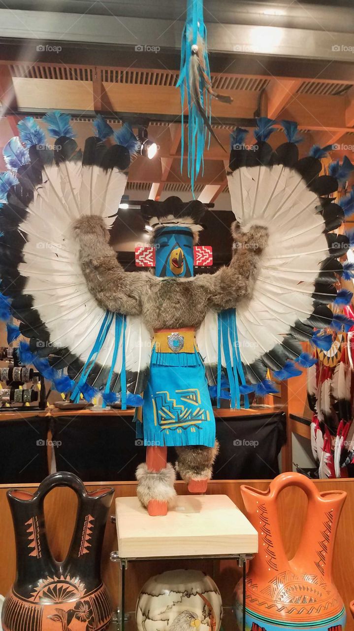 A large, winged Native American kachina doll made of wood, feathers, fur, and turquoise leather representing a god