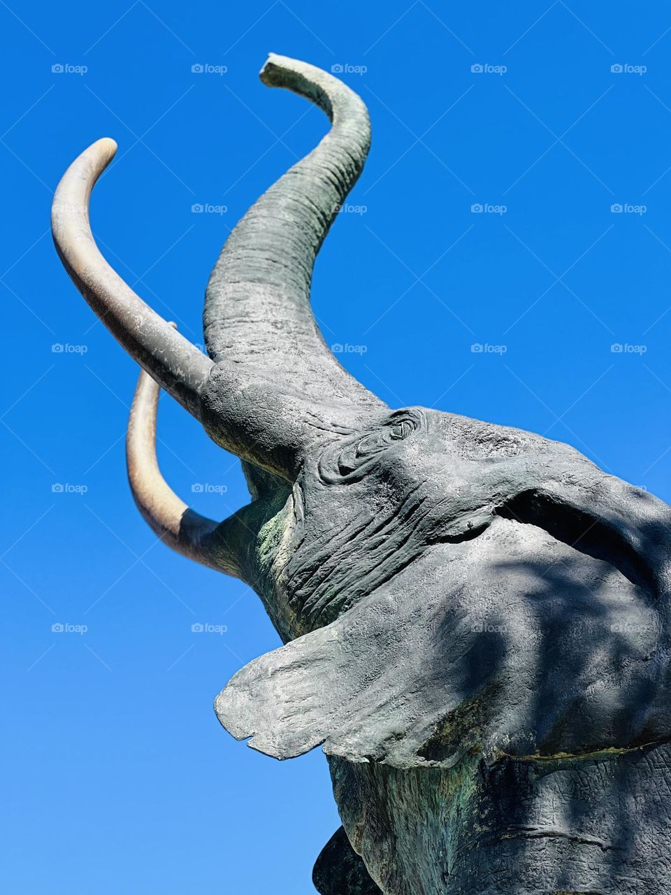 Closeup concrete statue of an elephant against a bright blue sky background 