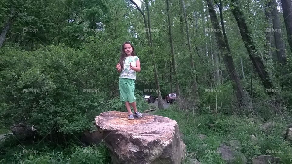 Girl blends in with nature standing on big, cool rock.