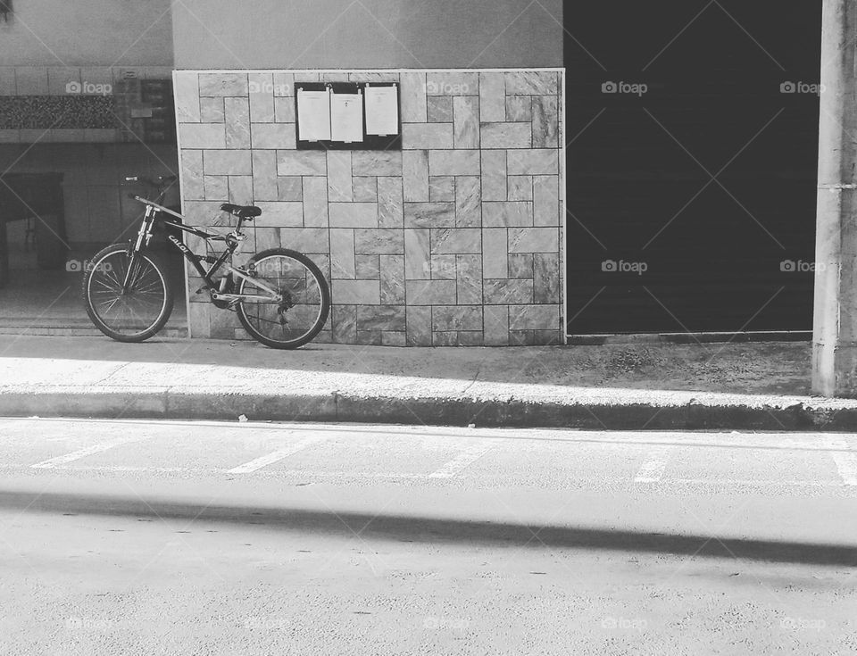 A bike by a wall where obituaries are put. A bar by the road