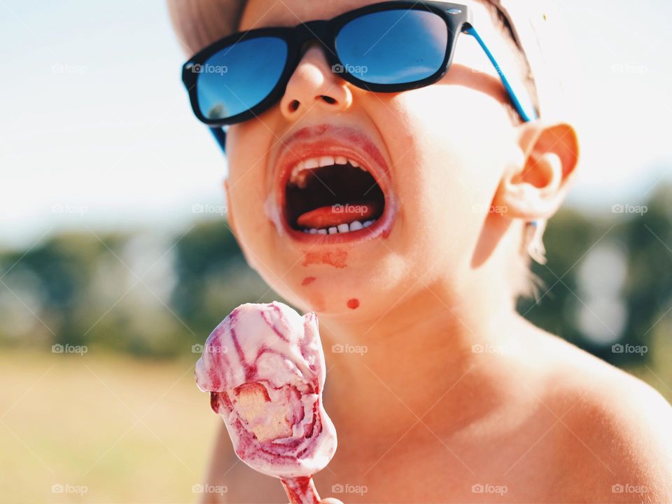 Kid wearing sunglasses enjoys an ice cream during a hot summer day 