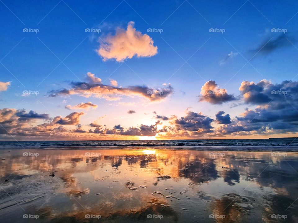 Beautiful landscape of sunrise over the ocean in the Brazilian state of Paraiba. Golden hour.  The sea, blue skies and the reflection of clouds on the wet sand of the beach.