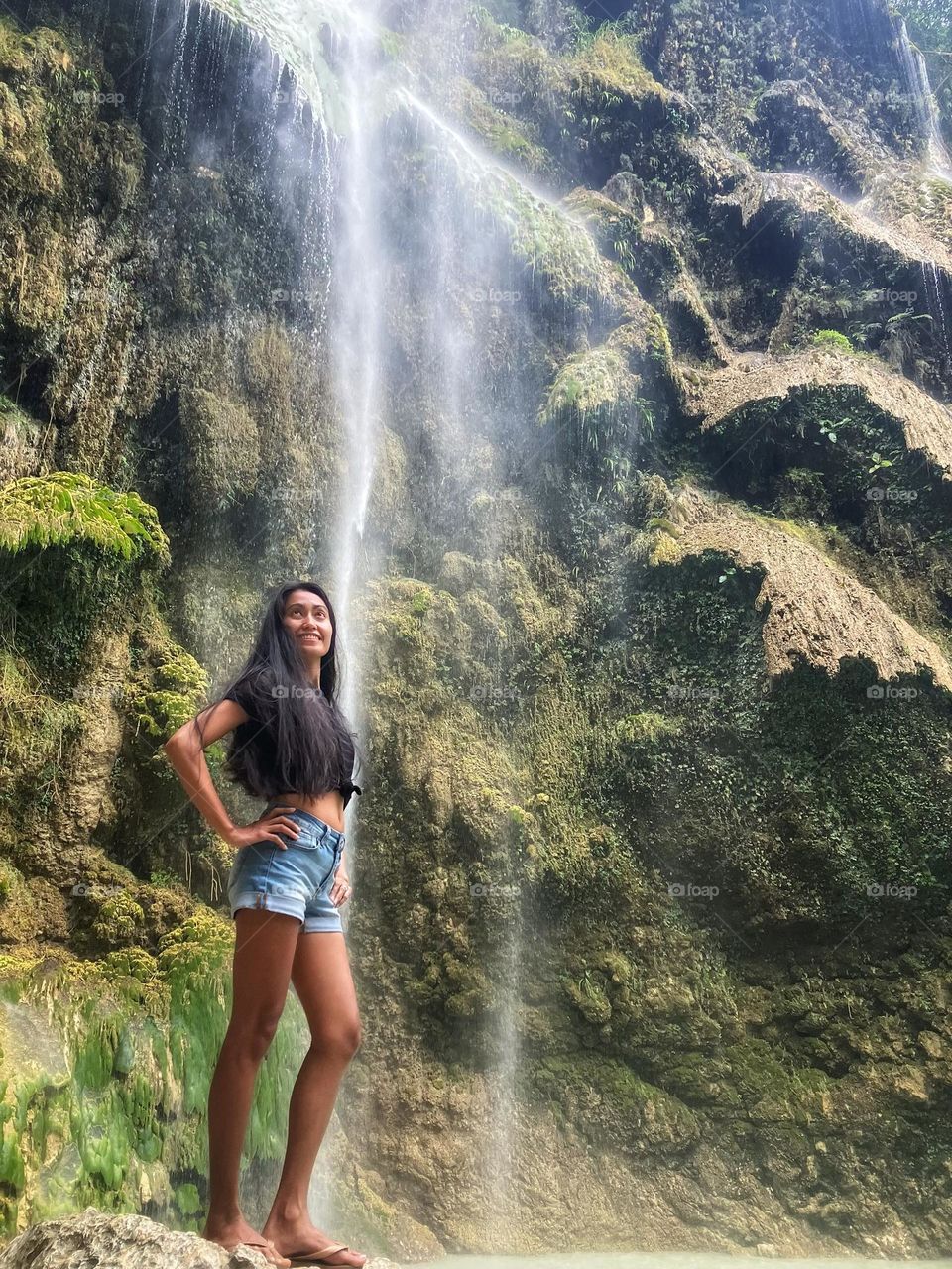 A woman standing on the rocks against a waterfall. Tumalog falls Oslob Cebu Philippines.