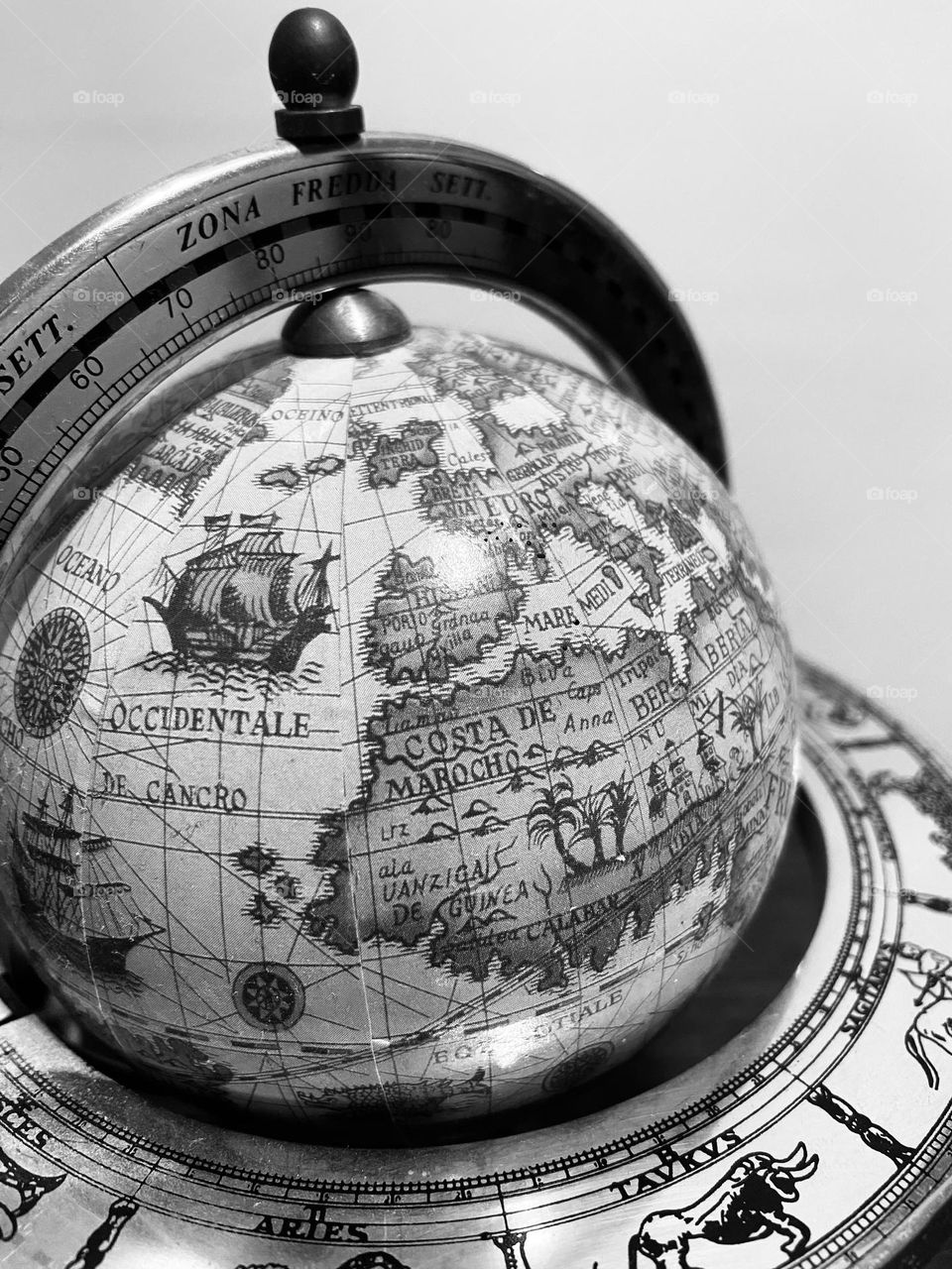 Black and white photo of an antique globe with horoscope signs around. 