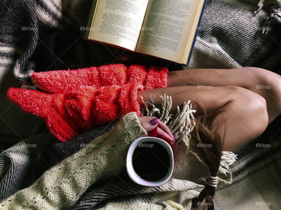 Overheard shot of a young woman enjoying her cup of coffee and favorite book in cozy bed